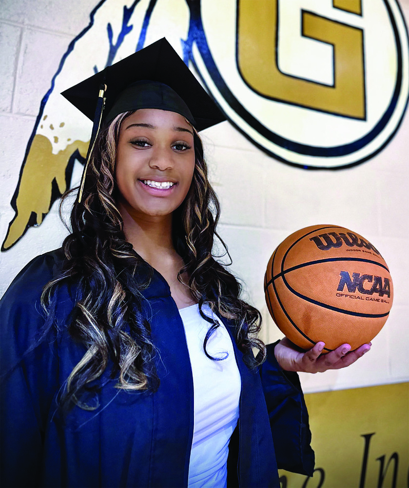 Diamynd Buckson posing in her cap and gown while holding a basketball in one hand.